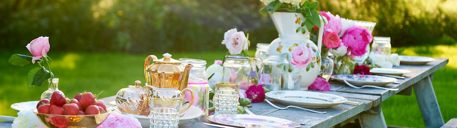 Close up of a luxury glamping picnic table laid with pretty pink floral crockery and flowers.