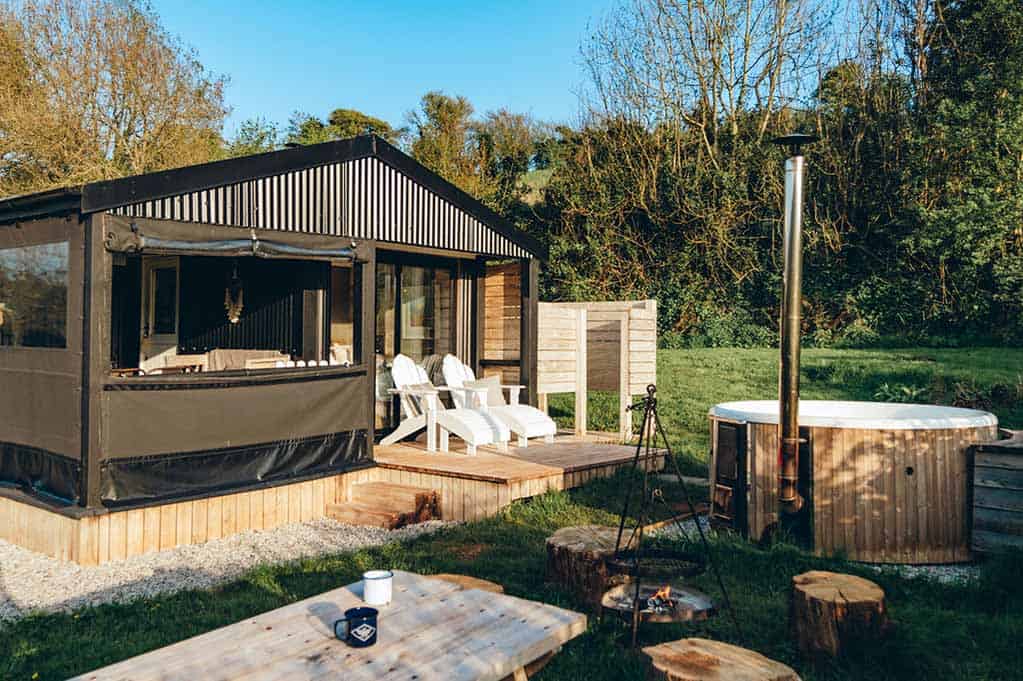 The Cabin at golden hour with the hot tub, fire pit, and picnic area all in view against the trees.